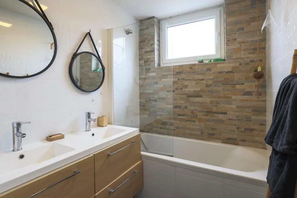 Salle de bain rénovée avec double vasque, mur en pierre et baignoire