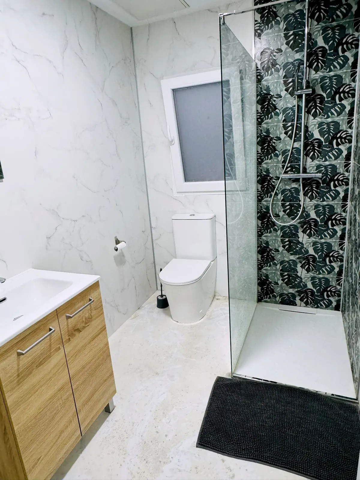 Salle de douche avec paroi en verre, carrelage effet marbre et papier peint tropical